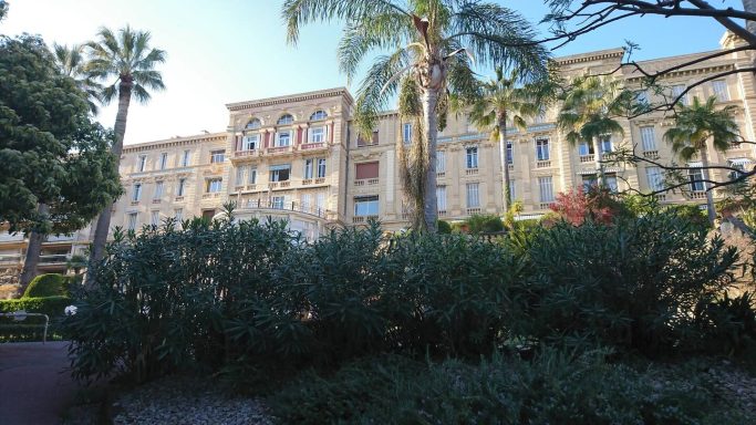 Bâtiment historique avec palmiers et jardin verdoyant devant lui.