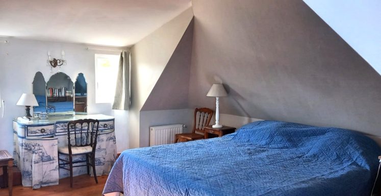 Chambre sous les combles avec lit, bureau, miroir et décoration simple.