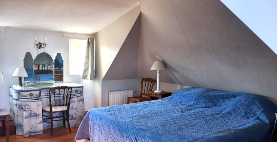 Chambre sous les combles avec lit, bureau, miroir et décoration simple.