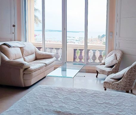 Salon lumineux avec canapé, fauteuils et vue sur la mer à travers des fenêtres.