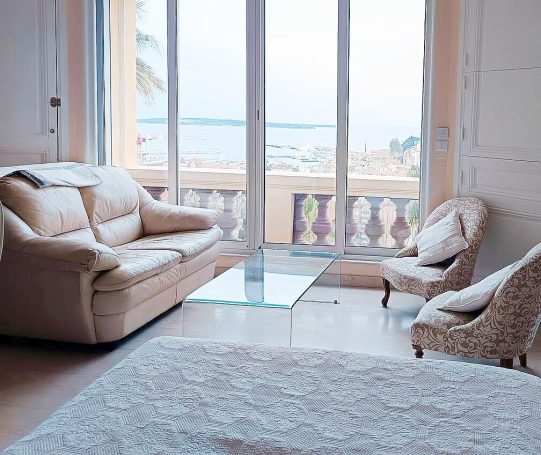 Salon lumineux avec canapé, fauteuils et vue sur la mer à travers des fenêtres.