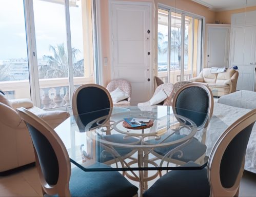 Intérieur lumineux avec une table en verre et des chaises, vue sur la mer.